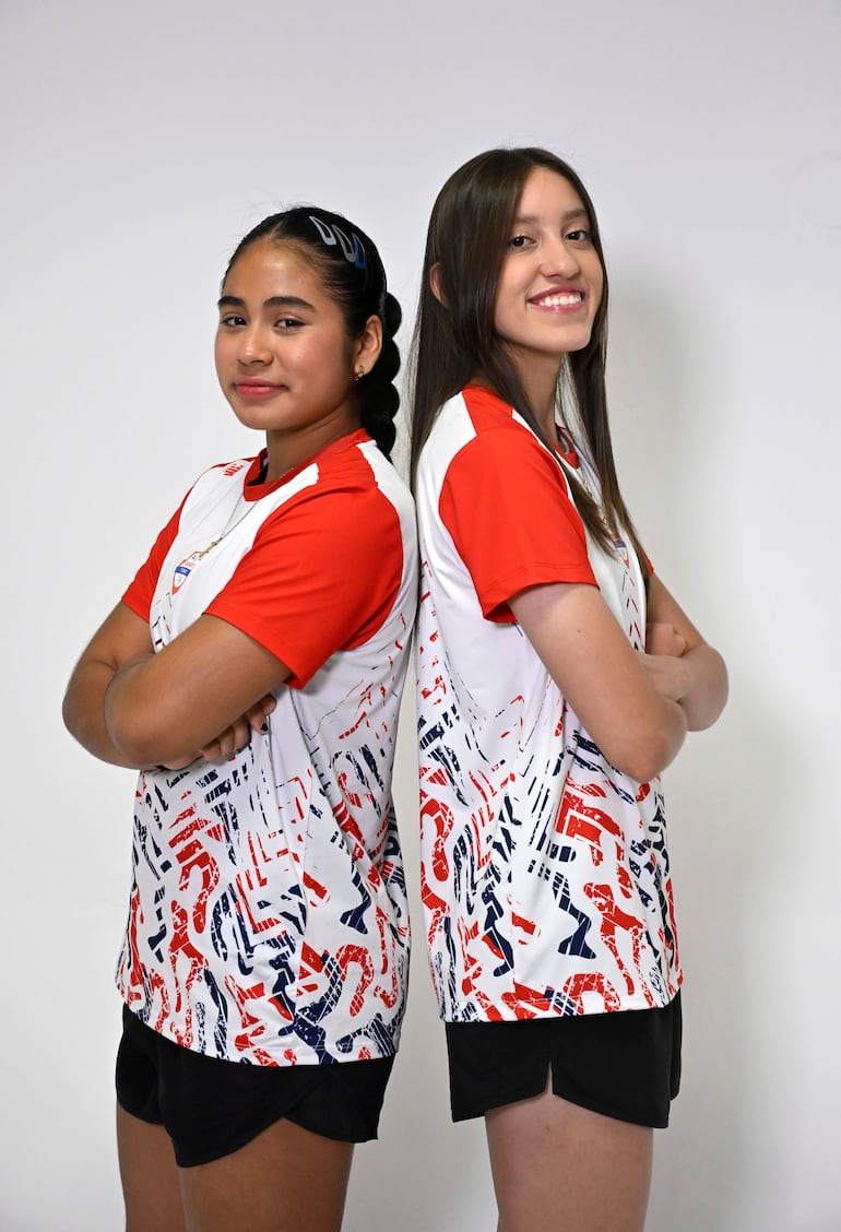 Sofía Martínez y Estefaía Gómez, con camisetas blancas con detalles rojos y azules, sonríen de pie en un fondo blanco.