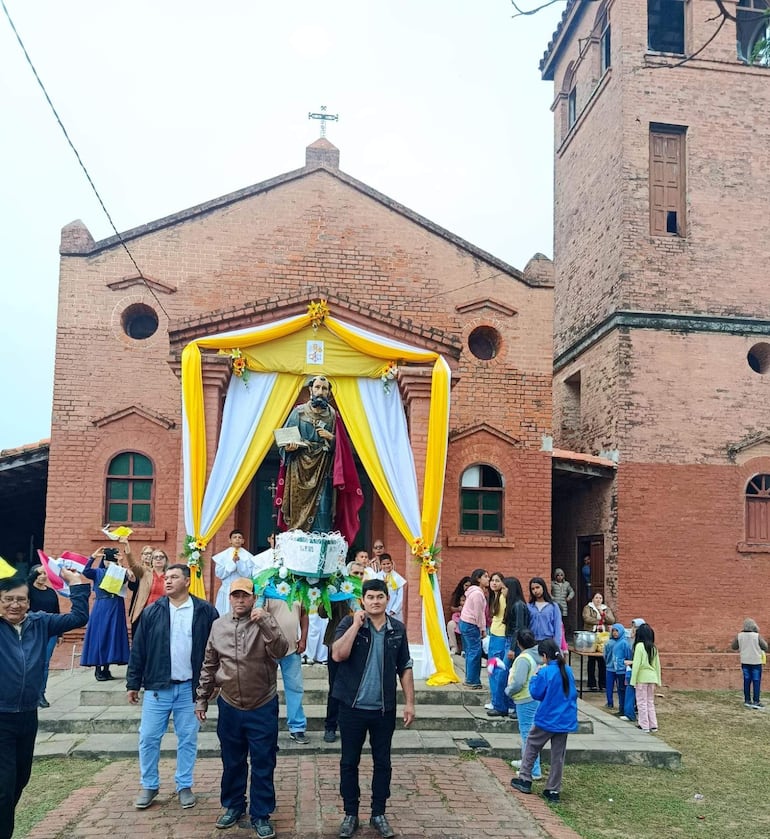 Grupo de personas en ropa variada levantando las manos en celebración frente a una iglesia decorada con flores.