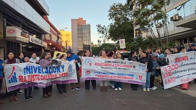 Mujeres manifestantes sosteniendo pancartas enérgicas sobre salario y derechos en una calle de Asunción, con un hombre en el centro sosteniendo un altavoz.