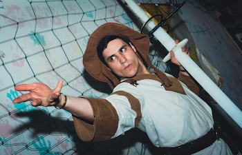 Joven vestido con atuendo medieval y sombrero de ala ancha, posando con una espada de plástico en un entorno informal.