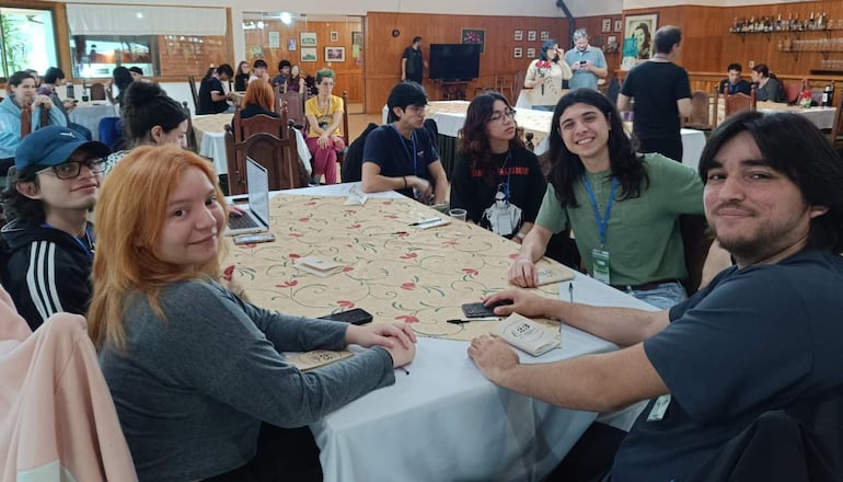 Jóvenes sonrientes se sientan alrededor de una mesa, creando un ambiente colaborativo y amistoso con decoración sencilla.