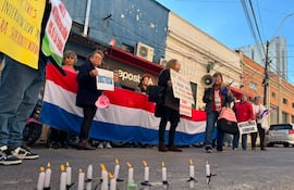 Mujeres con banderas de Paraguay y pancartas, algunas con velas encendidas, en una manifestación de jubilados en la calle.
