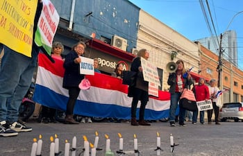 Mujeres con banderas de Paraguay y pancartas, algunas con velas encendidas, en una manifestación de jubilados en la calle.
