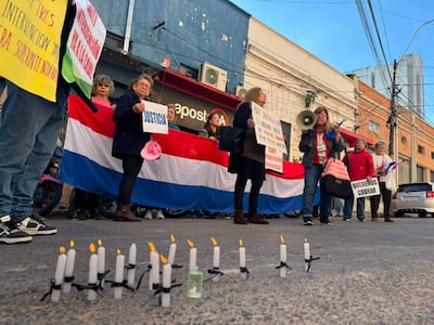 Mujeres con banderas de Paraguay y pancartas, algunas con velas encendidas, en una manifestación de jubilados en la calle.
