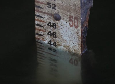 Medidor de nivel de agua parcialmente sumergido, con la escala marcada entre 40 y 52, visible en un entorno natural.
