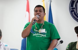 Oscar Reinaldo Martínez de pie con camiseta verde y micrófono, hablando mientras escucha el público en un ambiente con banderas.