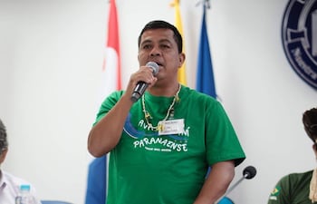 Oscar Reinaldo Martínez de pie con camiseta verde y micrófono, hablando mientras escucha el público en un ambiente con banderas.
