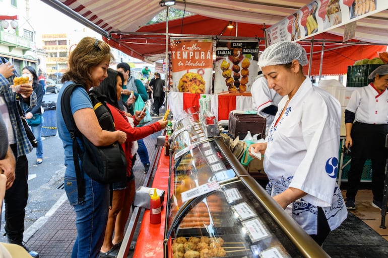 Gente comprando comida en un puesto en la plaza Liberdade. Destino turístico de São Paulo, Brasil.