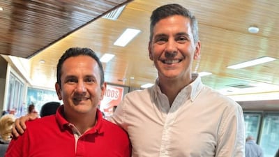 Hernán David Cubas con camiseta roja y Santiago Peña Santi con camisa blanca sonríen juntos en un ambiente con mesas y otras personas.