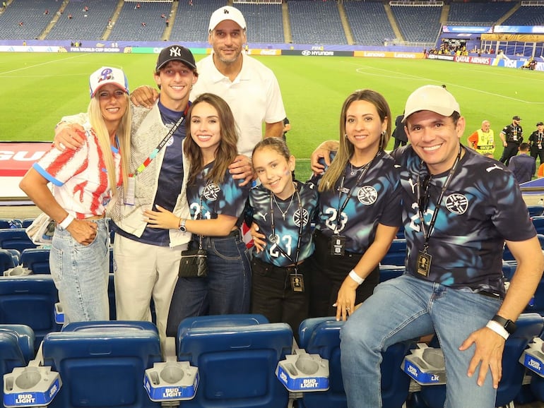 Matías Galarza sonríe con camiseta de fútbol mientras siete amigos posan felices en el estadio, rodeados de carteles de patrocinadores.