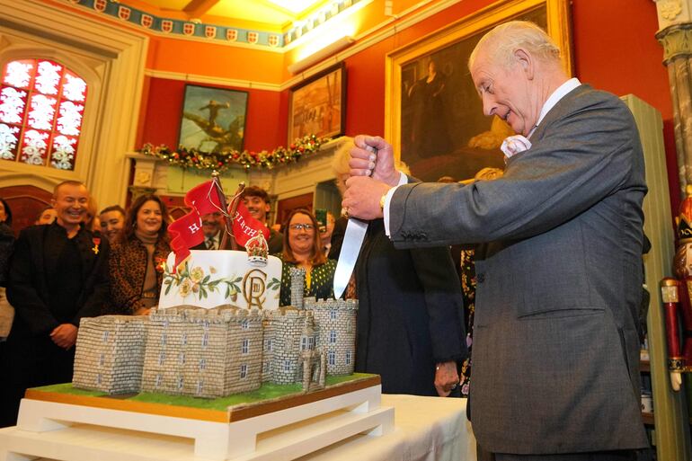 El rey Carlos III de Gran Bretaña se prepara para cortar un pastel con forma de castillo mientras él y la reina Camila asisten a una recepció para conmemorar el 200 aniversario del castillo de Cyfarthfa durante una visita a la ciudad de Merthyr Tydfil, en el sur de Gales, el 14 de noviembre de 2025, en el 77 cumpleaños del rey. (Kin Cheung / POOL / AFP)