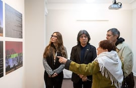 Mujer con bufanda blanca habla apasionadamente, acompañada de tres personas en una galería llena de obras artísticas.