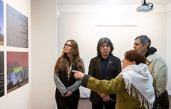 Mujer con bufanda blanca habla apasionadamente, acompañada de tres personas en una galería llena de obras artísticas.