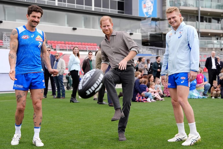 El príncipe Harry de Gran Bretaña patea un balón con los jugadores de la Liga Australiana de Fútbol (AFL) de los Western Bulldogs, Tom Liberatore y Adam Treloar, durante una visita a un evento de Movember en el Whitten Oval en Melbourne. (Jonathan Brady / POOL / AFP)