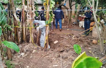 Hombre en traje de protección excavando en Caazapá, rodeado de policías que supervisan la escena con cintas amarillas de seguridad.