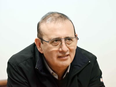 Erico Galeano Segovia sentado, con abrigo oscuro y gafas, mostrando una sonrisa serena en un entorno iluminado.