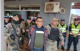 Elvio Benítez con chaqueta negra y roja, rodeado por agentes de seguridad en un ambiente tenso.
