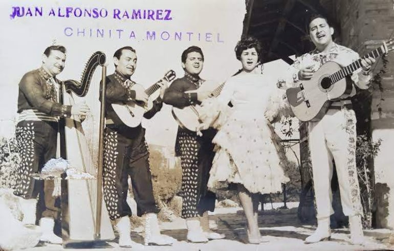 Juan Alfonso Ramírez y Chinita Montiel en trajes tradicionales, acompañados de guitarras y un arpa, en una celebración musical al aire libre.