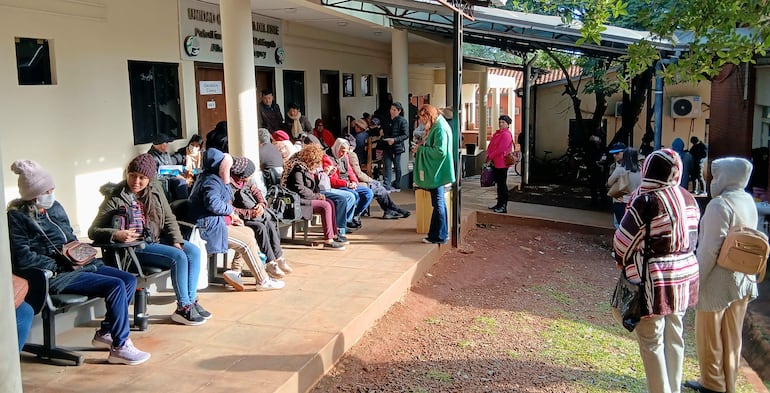 Grupo de personas, algunas con abrigos, conversan y esperan en la entrada del hospital bajo un clima frío.