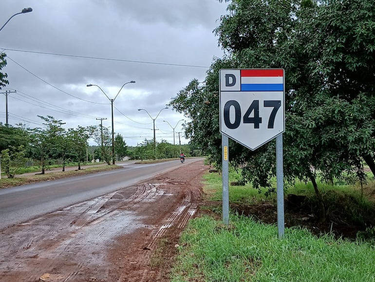 Señal de ruta D-047, rodeada de árboles y una carretera, bajo un cielo nublado y sin personas visibles.