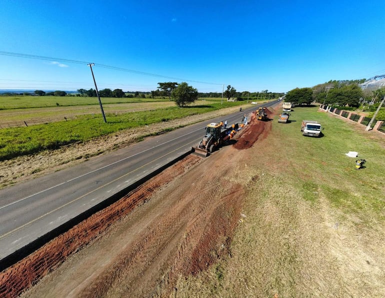 Cinco operarios en ropa de trabajo coordinan labores viales, rodeados de camiones y maquinaria pesada en un entorno rural.