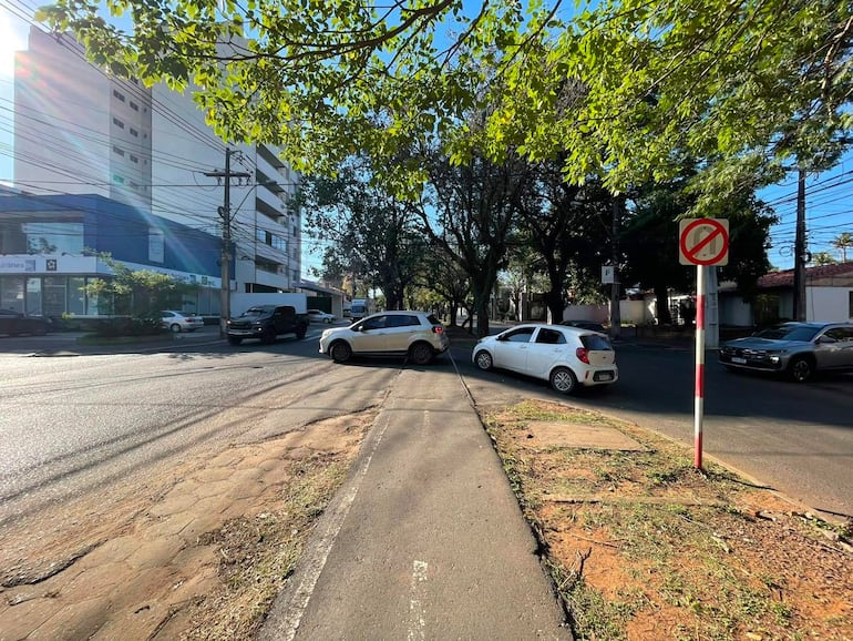 Intersección sin personas, varios autos en movimiento, edificios residenciales y comerciales al fondo.