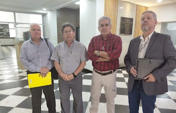 Cuatro hombres en un ambiente interior, con prendas formales y documentos en mano, discuten con calma sobre jubilaciones.