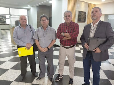 Cuatro hombres en un ambiente interior, con prendas formales y documentos en mano, discuten con calma sobre jubilaciones.
