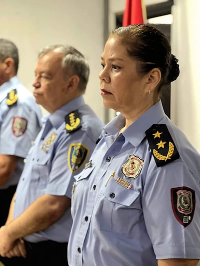 María Rossana Chávez Leal en camisa azul de policía con expresión seria, flanqueada por hombres en uniforme escuchando atentamente.