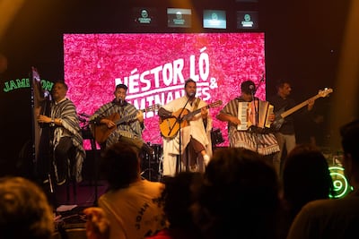 Cinco músicos en el escenario, con vestimentas tradicionales. Tocado el arpa, guitarras y acordeón en un ambiente festivo.