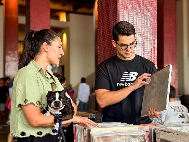 Mujer con cabello recogido y vestimenta verde sostiene un perro en un mercado con luces cálidas y ambiente moderno.