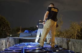 Tres agentes de Policía Antinarcóticos en camisetas negras realizan una operación nocturna junto a barriles azules en un camión.