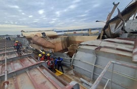 Personas con cascos amarillos y chalecos de salvavidas inspeccionan un barco dañado en un puerto, en un entorno de emergencia.