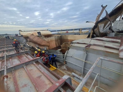 Personas con cascos amarillos y chalecos de salvavidas inspeccionan un barco dañado en un puerto, en un entorno de emergencia.