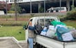 Soledad Núñez con chaleco gris y camisa de mezclilla, manipulando bolsas de basura en un evento comunitario al aire libre.