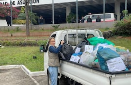 Soledad Núñez con chaleco gris y camisa de mezclilla, manipulando bolsas de basura en un evento comunitario al aire libre.