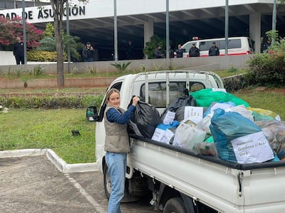 Soledad Núñez con chaleco gris y camisa de mezclilla, manipulando bolsas de basura en un evento comunitario al aire libre.