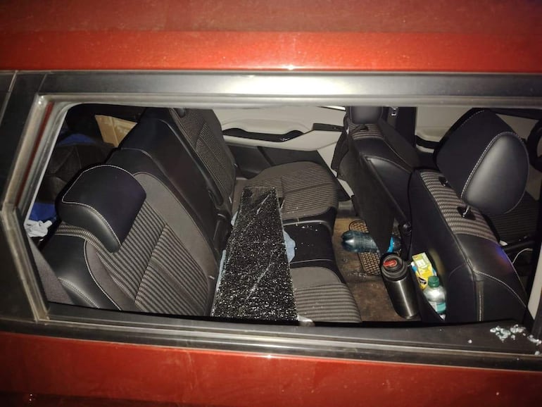 Interior de un automóvil rojo con cristal roto en el suelo, mostrando signos de haber sido vandalizado.