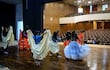 Seis mujeres en faldas tradicionales de colores vivos ensayan danza en escenario moderno, con asientos vacíos al fondo.