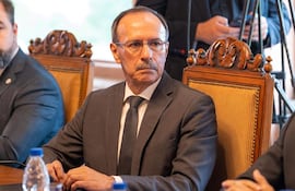 Óscar González en traje oscuro y corbata, con expresión seria, sentado en sala de reuniones junto a otro hombre parcialmente visible.