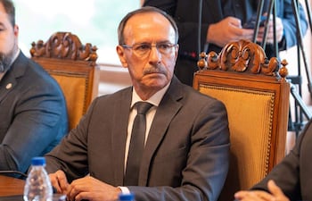 Óscar González en traje oscuro y corbata, con expresión seria, sentado en sala de reuniones junto a otro hombre parcialmente visible.