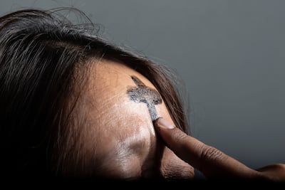 Un sacerdote marca la frente de una mujer con una cruz de ceniza.