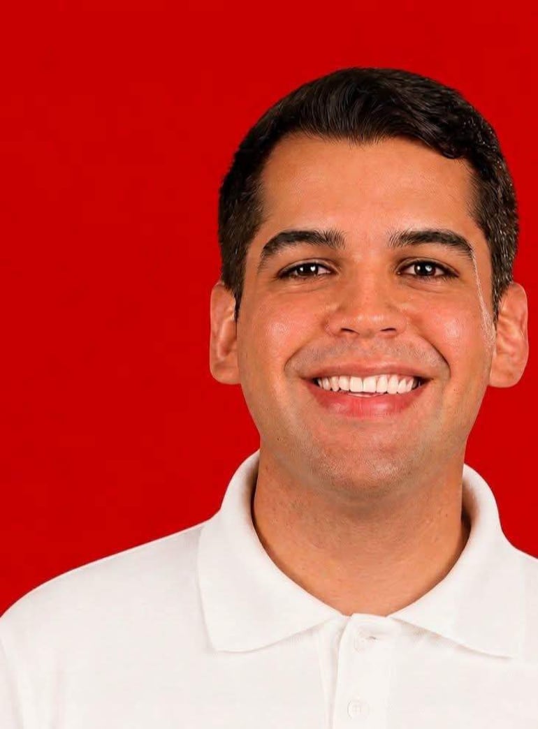 Persona sonriente con cuello visible, fondo difuso que sugiere un ambiente festivo.