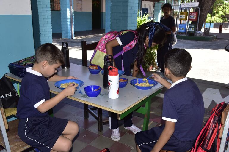 Niños almuerzan sobre una mesa improvisada en la entrada misma de la escuela Juan Manuel Frutos.