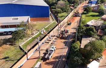 Escena de obras viales en Avelino Martínez con vehículos de trabajo y un edificio azul de arquitectura moderna de fondo.