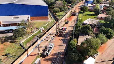 Escena de obras viales en Avelino Martínez con vehículos de trabajo y un edificio azul de arquitectura moderna de fondo.