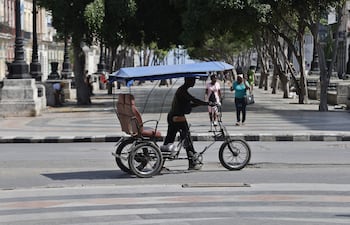Una persona camina con un bicitaxi, en La Habana (Cuba).