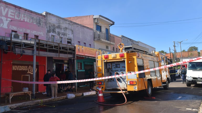 Camión de bomberos amarillo en la calle, personas observando la situación. Cinta delimita el área de emergencia.