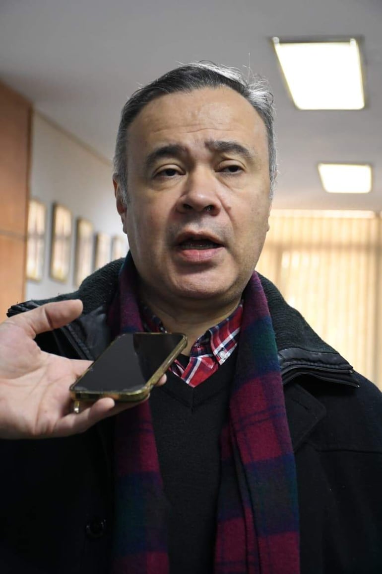 Humberto Blasco en abrigo negro y bufanda morada y verde, hablando con expresión de atención, mientras sostiene un teléfono móvil.