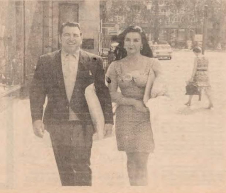 Luis Alberto del Paraná en traje oscuro conversa con Isabel Sarli, vestida con un vestido claro, en una calle urbana.